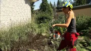 Sandra geht mit einer Motorsäge gegen die Sträucher im Garten vor