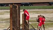 Members of the Red team attempt to climb a hurdle in a physically challenging section of an obstace course.