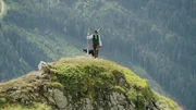 Auf einem Hügel steht ein Hirte mit seinem Collie