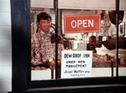 Ike (Joe Conley) stellt ein Plakat in das Schaufenster, auf dem die Neueröffnung des Dew Drop Inn angekündigt wird. Jason hatte das Lokal gekauft und will es nun selbst betreiben.