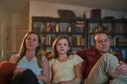 Hannahs Eltern Amanda (Jo Hunt, l.) und Steve (Mark Saturno, r.) versuchen Hannah (Evie MacDonald, M.) beim Fernsehgucken auf anderen Gedanken zu bringen.