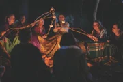 Natalie (Nandini Rajagopal, h.2.v.l.), Hannah (Evie MacDonald, h.3.v.l.), Olivia (Elena Liu, h.M.), Sarah (Jake Childs, h.r.) und andere Mitschülerinnen sitzen gemeinsam beim Lagerfeuer. Noch ahnt Hannah nicht, welche intimen Fragen einige von ihnen ihr stellen werden.