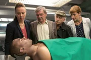 Dr. Rosalind Schmidt (Helene Grass, r.) teilt Vicky (Katja Danowski, l.), Günter (Wolfgang Winkler, 2.v.l.) und Edwin (Tilo Prückner, 2.v.r.) das Ergebnis der Obduktion mit. Connor Taylor (Roy Wesche, vorne) ist an einem Herzinfarkt gestorben.