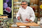 Starkoch Hans Jörg Bachmeier salzt Fisch auf einem Holzbrett.