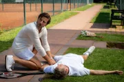 Hans-Jürgen Wagenburg (Vivian Frey, l.) findet den Tennislehrer (Christian David Gebert, r.) des Tennisclubs tot neben dem Tennisplatz vor.