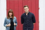 Amy Bruni and Adam Berry pose in front of a painted red door.