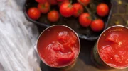 Fresh cherry tomatoes (on the vine) and two open cans of tomatoes on a kitchen counter