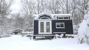 Snow flurries gently fall to the ground and cover Jesse and Nora's completed tiny house and traveling theater, on a blustery winter day, in Richmond, Rhode Island, as seen on Tiny House, Big Living