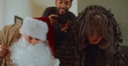 Andi (Milan Peschel, l.) ist als Weihnachtsmann verkleidet und überreicht mit Rocco (Hoang Minh Ha, r.) als Knecht Ruprecht der kleinen Frida ihre Weihnachtsgeschenke. Theo (Benito Bause) filmt das Geschehen.