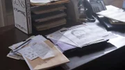 Paperwork including a gun book and police sketch of Nicholas Scarseth scattered around a desk.
