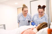 Praxisanleiterin Irene mit der angehenden Pflegefachkraft Kyra (r) bei einer Patientin.
