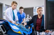 Dr. Matteo Moreau (Mike Adler, r.) findet vor dem Haupteingang die junge und nicht mehr ansprechbare Frau Sunny Schneider (Komparsin) und bringt sie in die Notaufnahme zu Dr. Mikko Rantala (Luan Gummich, l.) und Florian Osterwald (Lion Wasczyk, M.).