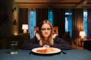 Floor (Bobbie Mulder) sitzt am Tisch während Kees über ihr Abendessen vloggt.