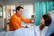 Neiss (Patrick Kalupa) sitzt am Bett von Andrea Wellenbrink (Anja Antonowicz) und füttert sie, da sie ihre Arme nicht bewegen kann.