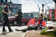 Melanie (Sanna Englund, l.) und Mattes (Matthias Schloo, 2.v.l.) ermitteln im Falle einer Fahrerflucht, während Notarzt Haase (Fabian Harloff, r.) und ein Kollege (Komparse) den verletzten Beifahrer (Bert Tischendorf, liegend) versorgen.