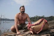 Hazen hockt neben einem Korb am Ufer des Mekong.
