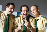 Martin Riedl (Paul Sedlmeir, l.), Johannes Staller (Helmfried von Lüttichau, M.) und Sonja Wirth (Anett Fleischer, r.) amüsieren sich mit einem Handy.