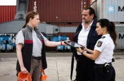 Arda (Yasemin Cetinkaya) und Jäger (Markus John) gehen durch gestapelte Container und treffen auf Karin Uhr (Katharina Abel, l.).