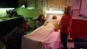 Kathleen sitzt neben Rlies, der in einem Krankenhausbett liegt.