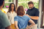 Martin Klausen (Peter Trabner, r.) erklärt der Elterngruppe, wie zum Beispiel Yaa (Rebecca Lina Wilson-Kamm, l.) und Nina (Lavinia Wilson, M.), wie autoritäre Erziehung funktioniert, obwohl sie eigentlich einen Workshop zu Mediation gebucht hatten.