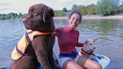 Pia mit Neufundländer „Justus“ und Corgi-Mischling „Feeline“ auf einem Stehpaddelbrett am Rothsee. Für Feeline ist es das erste Mal im Wasser.