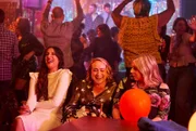 Die Party ist ein voller Erfolg. Während die anderen auf der Tanzfläche feiern, sitzen Rana (Taj Atwal, l.), Toni (Leah Brotherhead, M.) und Paula (Sinead Matthews, r.) zusammen und genießen die ausgelassene Stimmung.