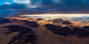 Kamel mit gefiederten Belgleitern im abendlichen Wadi Rum-Tal in Jordanien. Das Wadi Rum-Schutzgebiet in Jordanien gehört zum Weltnaturerbe der UNESCO.