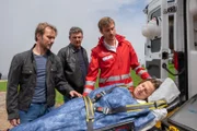 Nach Ina Lechners (Maria Simon, liegend) Zusammenbruch macht sich nicht nur Jan Seidl (Max Woelky, l.) Sorgen, auch Dr. Martin Gruber (Hans Sigl, M.) ist beunruhigt. Sanitäter David (Frédéric Brossier, r.) sorgt dafür, dass sie schnellstmöglich in die Klinik gebracht wird.
