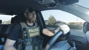 HSI-Agent Connor am Steuer seines Fahrzeugs, während er eine kugelsichere Polizeiweste trägt. (Kredit: National Geographic)
