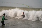Kanur, India - Gordon Ramsay (R) battles strong waves while drag net fishing.  (Credit: National Geographic/Justin Mandel)