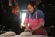 Mrs. Wang makes momo - bread - with smoked yak meat and pork hanging in the background.