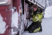 Eirik arbeitet daran, Ketten an den Rädern eines Lastwagens zu befestigen, damit er auf den vereisten Straßen besser greifen kann. (National Geographic)