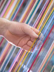 Worker adjusting multicoloured silk yarn on industrial loom in textile mill