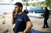 Frank van Dijk (Niklas Osterloh, v.) telefoniert, währen die Leiche abtransportiert wird (mit Komparsen).