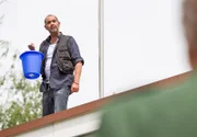Yazid (Hannes Ringlstetter) schüttet einen ersten Eimer mit blau gefärbtem Wasser aufs Dach.