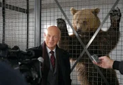 Vor dem Bärenkäfig ist "der Bär" los. Vor laufenden Kameras erklärt Staatssekretär Bredow (Dietrich Hollinderbäumer) der Presse stolz, dass es nur seinem Einsatz zu verdanken ist, dass der Braunbär nicht getötet, sondern gefangen und gesundgepflegt wurde. Er kann wieder ausgewildert werden.