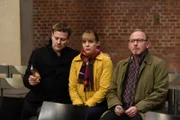 Das Trio Harald Neuhauser (Marcus Mittermeier), Angelika Flierl (Bernadette Heerwagen) und Ludwig Schaller (Alexander Held) sitzen in der Friedhof-Aussegnungshalle und beobachten die Gäste.