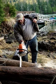 PORT PROTECTION, ALASKA- Tim "Curly" Leach saws a log in Port Protection. (Photo Credit: National Geographic Channels/ Rocco Colonna)