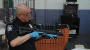 CBP-Beamter Cisneros hält eine Waffe in der Hand, die in einem verschickten Paket in der Poststelle des JFK International Airport gefunden wurde, während er erklärt, warum eine orangefarbene Spitze an gefälschten Feuerwaffen angebracht sein muss.