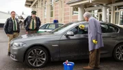 Hubert (Christian Tramitz, l.) und Staller (Helmfried von Lüttichau, M.) parken auf dem Gelände des Spielzeugherstellers Stark und treffen auf den Hausmeister (Komparse, r.), der die verdreckte Windschutzscheibe einer Limousine abwäscht.