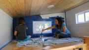 Tiny house owner and builder Sheradan Pate works with her daughter Sage to paint an accent wall in her loft using blue chalkboard paint, as seen on Tiny House, Big Living.