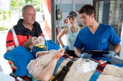 Maria Köhser (Valerie Sophie Körfer, v. mit Komparse, l.) wird nach einem Fahrradsturz ins Johannes-Thal-Klinikum gebracht. Julia Berger (Mirka Pigulla, M.) hat die junge Braut notversorgt und übergibt sie in der Notaufnahme an Ben Ahlbeck (Philipp Danne, r.).