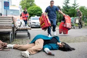 Dr. Elias Bähr (Stefan Ruppe, h.M. mit Komparsen) eilt seiner Ex-Frau Ameena Schneider (Mira Mazumdar, v.) zur Hilfe.