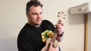 Shaun at home holding a Ukulele.