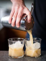Two cocktails being poured into iced glasses