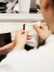 Cropped image of female chef reading order tickets in commercial kitchen
