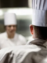 A closeup view from behind of a chef wearing a toque hat in a commercial kitchen.