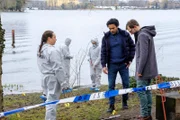 Eine junge Frau wird vermisst. Am See findet Spusi Jutta Specht (Gabriele Völsch, l.) das Handy der Vermissten und entdeckt Kampfspuren. Doch was den beiden Kommissaren David Grünbaum (Omar El-Saeidi, M.) und Christoph Westerman (Hendrik von Bültzingslöwen, r.) besonders auffällt: die Spuren eines Fat-Bikes. Im Hintergrund zwei Komparsen in weißen Overalls.