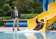 Hubert (Christian Tramitz, links) staunt, als Staller (Helmfried von Lüttichau) hinter einem Toten von der Wasserrutsche ins Becken schlittert.