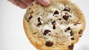 Hand dipping large chocolate chip cookie in small coffee cup